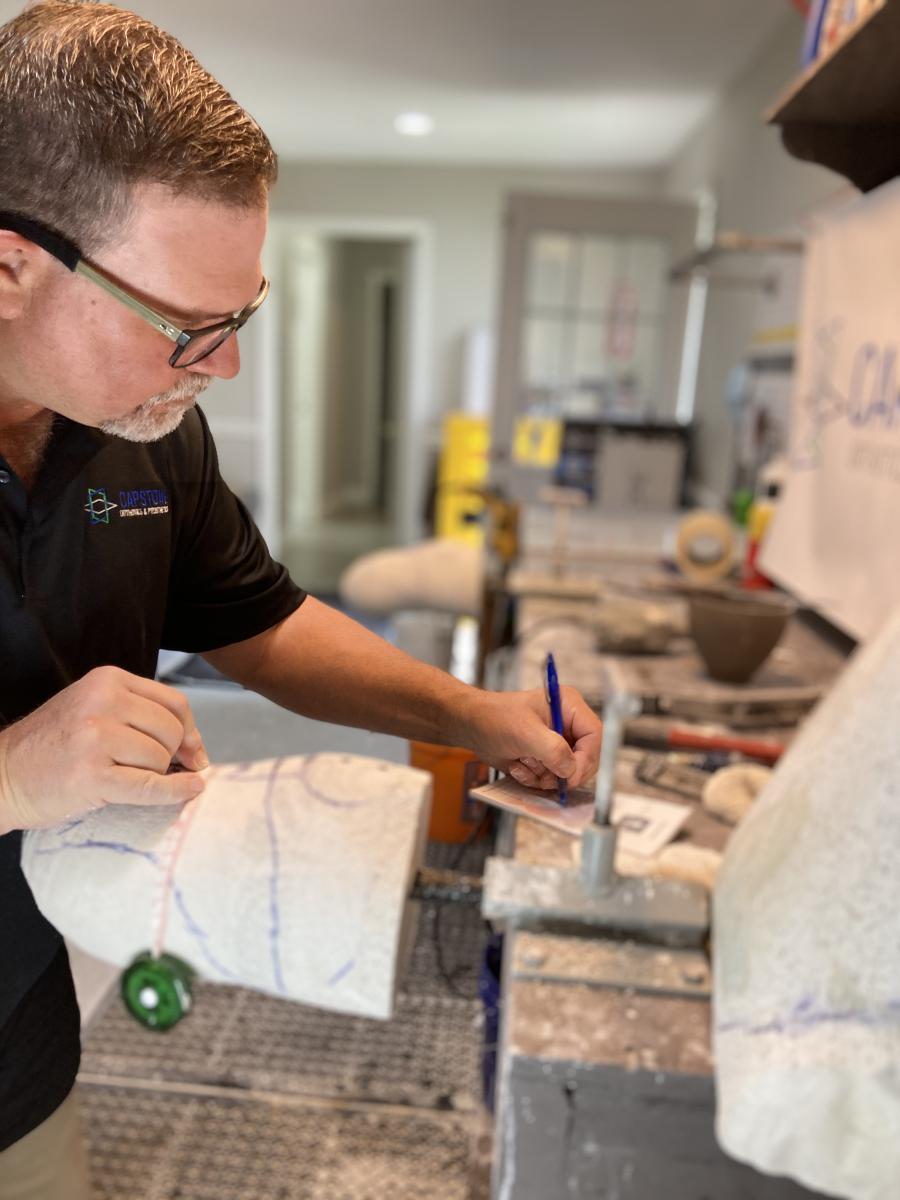 Male clinician modifying a plaster below knee prosthetic mold and writing down measurements to a notepad