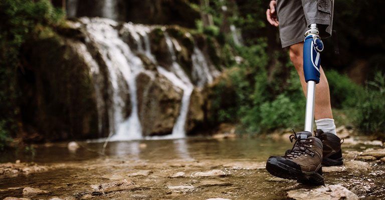 Image of man with prosthetic leg walking outside in nature with waterfall in background