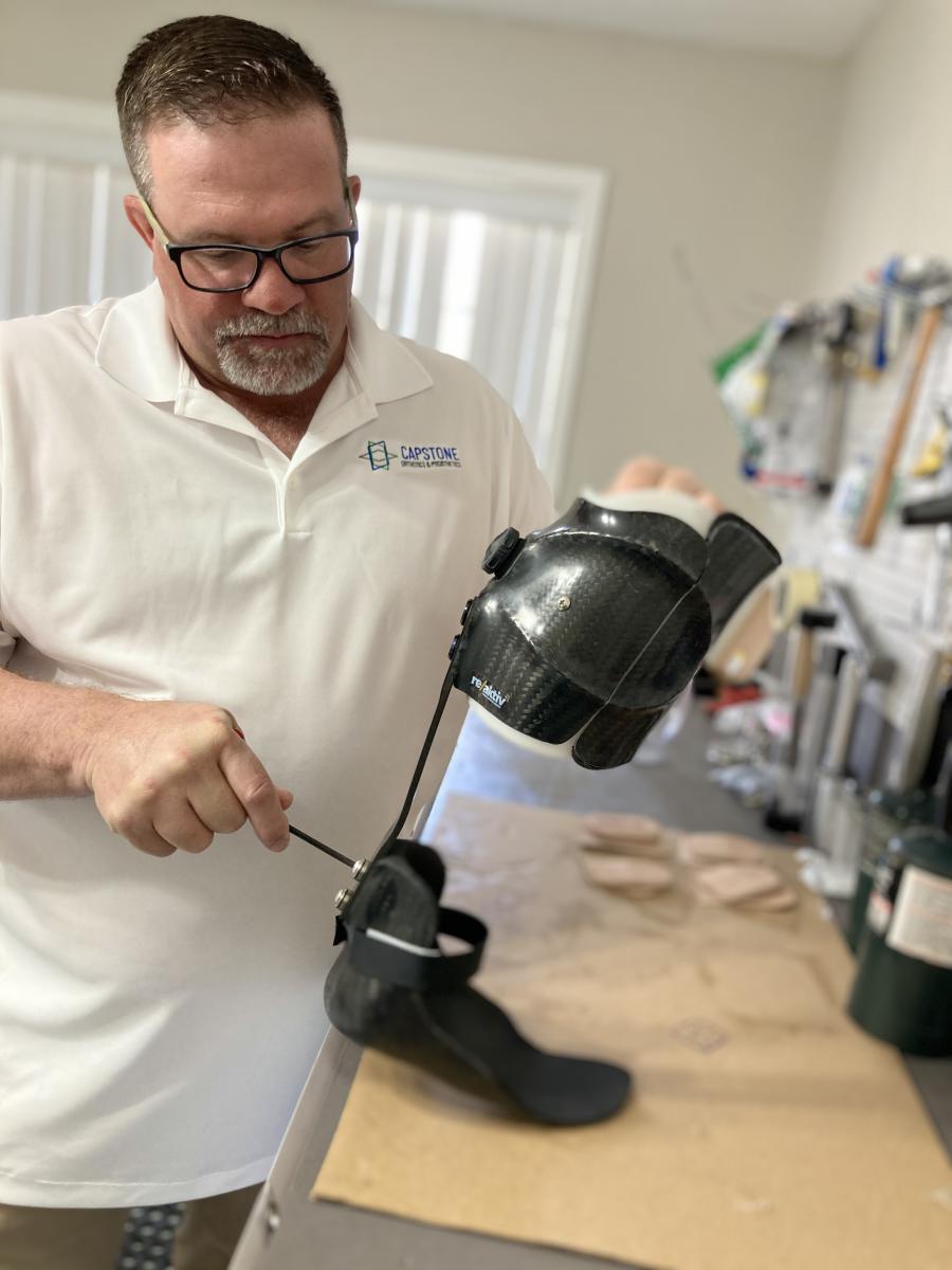 Male clinician tightening the back screw on the strut of a carbon fiber ReAktiv AFO on a workbench