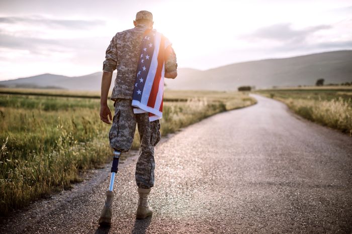 Soldier with prosthetic leg walking away with American flag over his shoulder