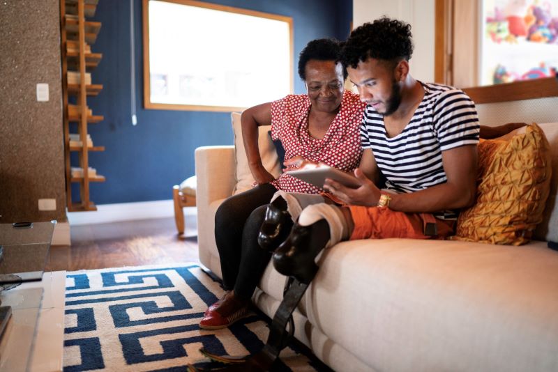 Young man with two prosthetic legs showing mother tablet